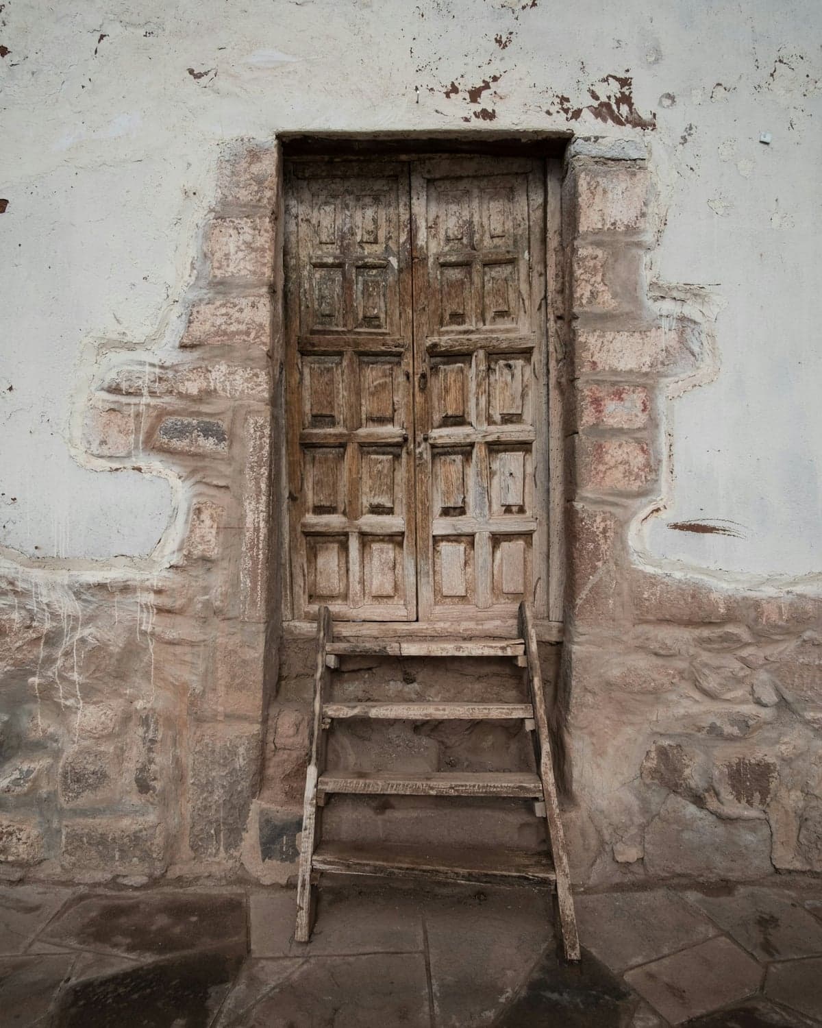 Antigua puerta tallada de madera con escalera, fachada de adobe en pueblo andino